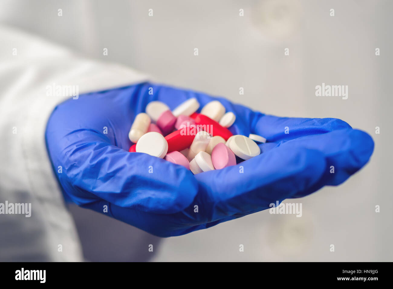 Doctora con la mano llena de diversas pastillas y medicamentos, cerca del profesional médico en bata blanca y guantes de protección Foto de stock
