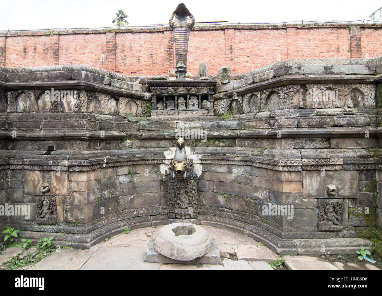 Pared del estanque de un templo en Katmandú mostrando tallas en piedra, una protección de rey cobra y una boquilla de agua de bronce tallado Foto de stock
