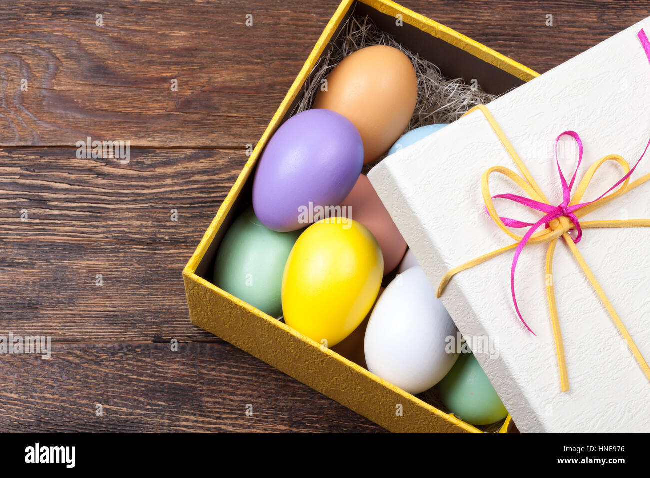 Colorida decoración de huevos de Pascua en la hermosa caja de regalo con cintas sobre fondo de madera Foto de stock