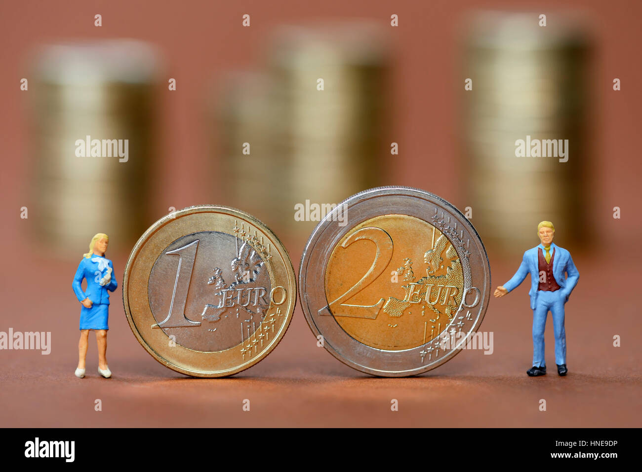Figuras en miniatura del hombre y de la mujer junto a un uno y dos monedas euro simbólico, foto de la desigualdad salarial, Miniaturfiguren von Mann und Frau neben Ein- u Foto de stock