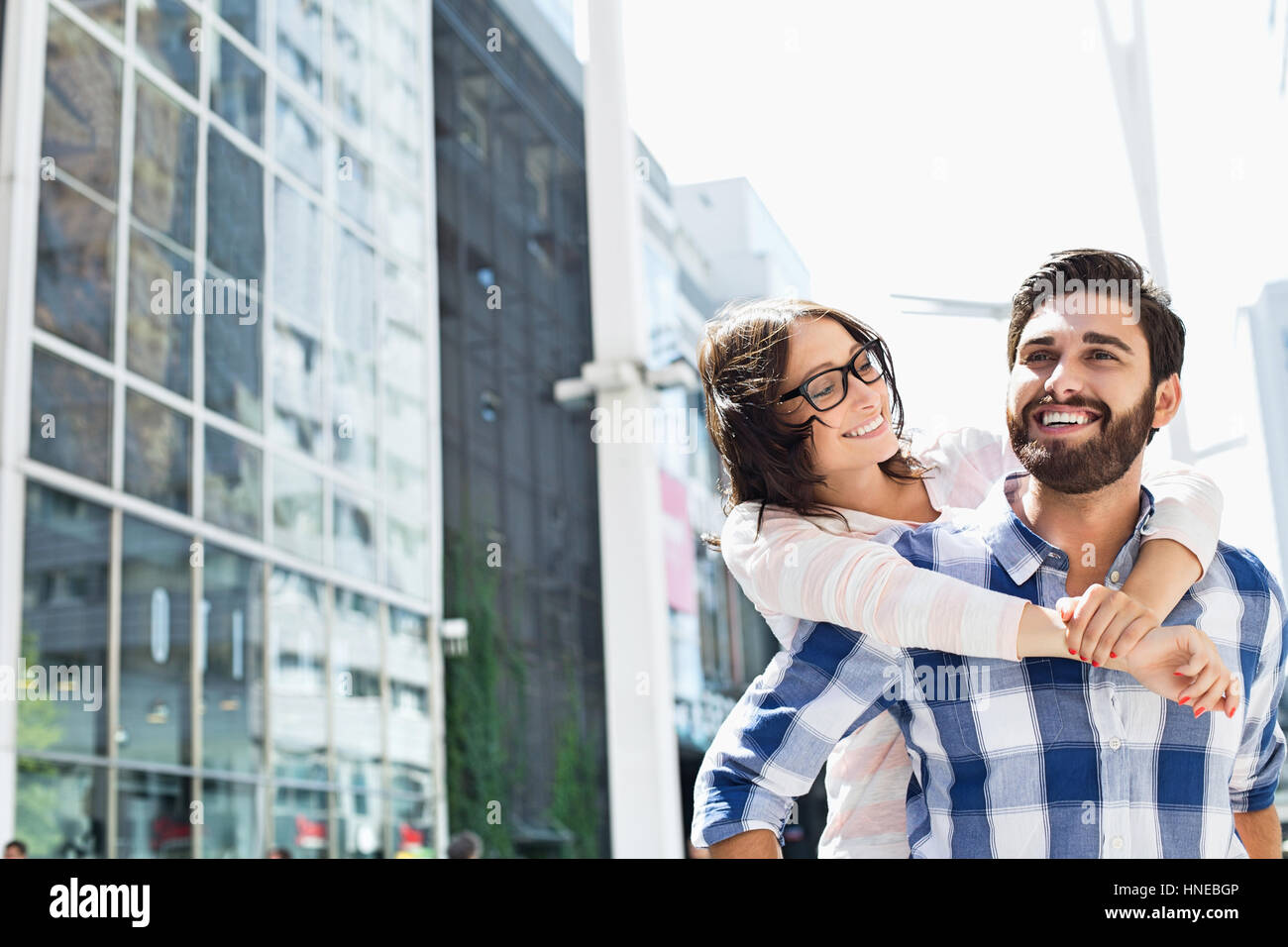 Hombre feliz viaje piggyback dando a la mujer en la ciudad Foto de stock