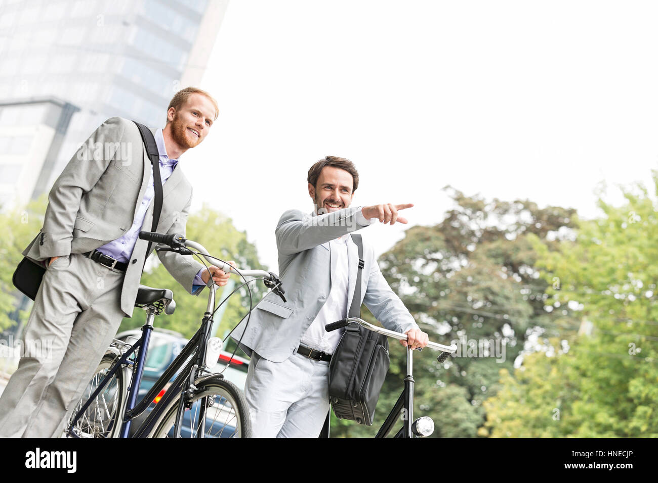 Empresario sonriente con bicicleta mostrando algo a un colega en la calle Foto de stock