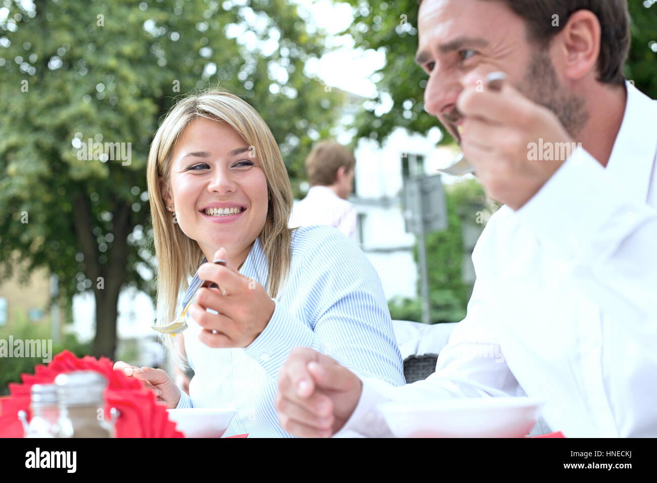 Feliz empresaria comiendo alimentos con su colega en el café en la acera Foto de stock