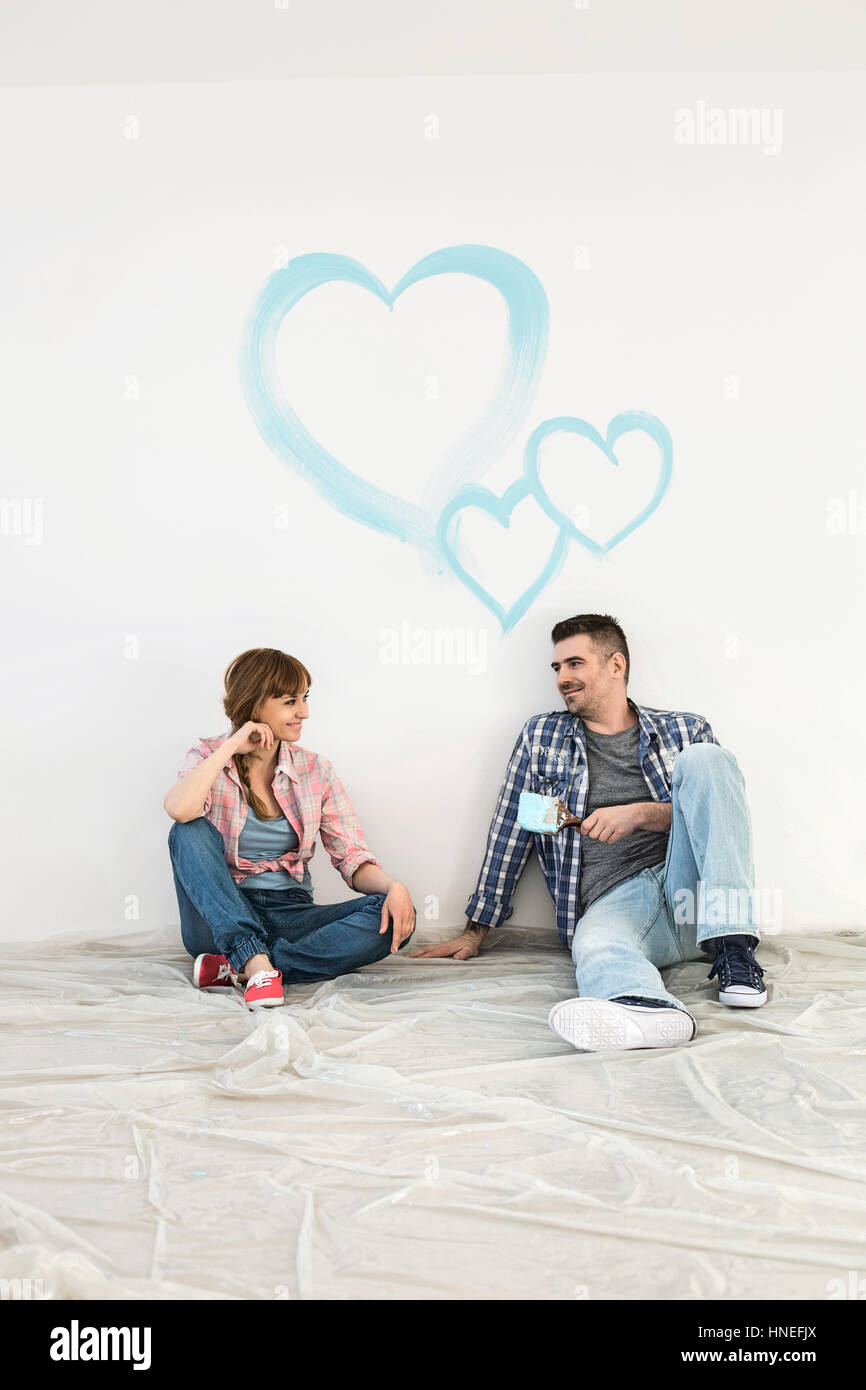 Longitud completa de mediados de-pareja adulta con corazones pintados en la pared Foto de stock