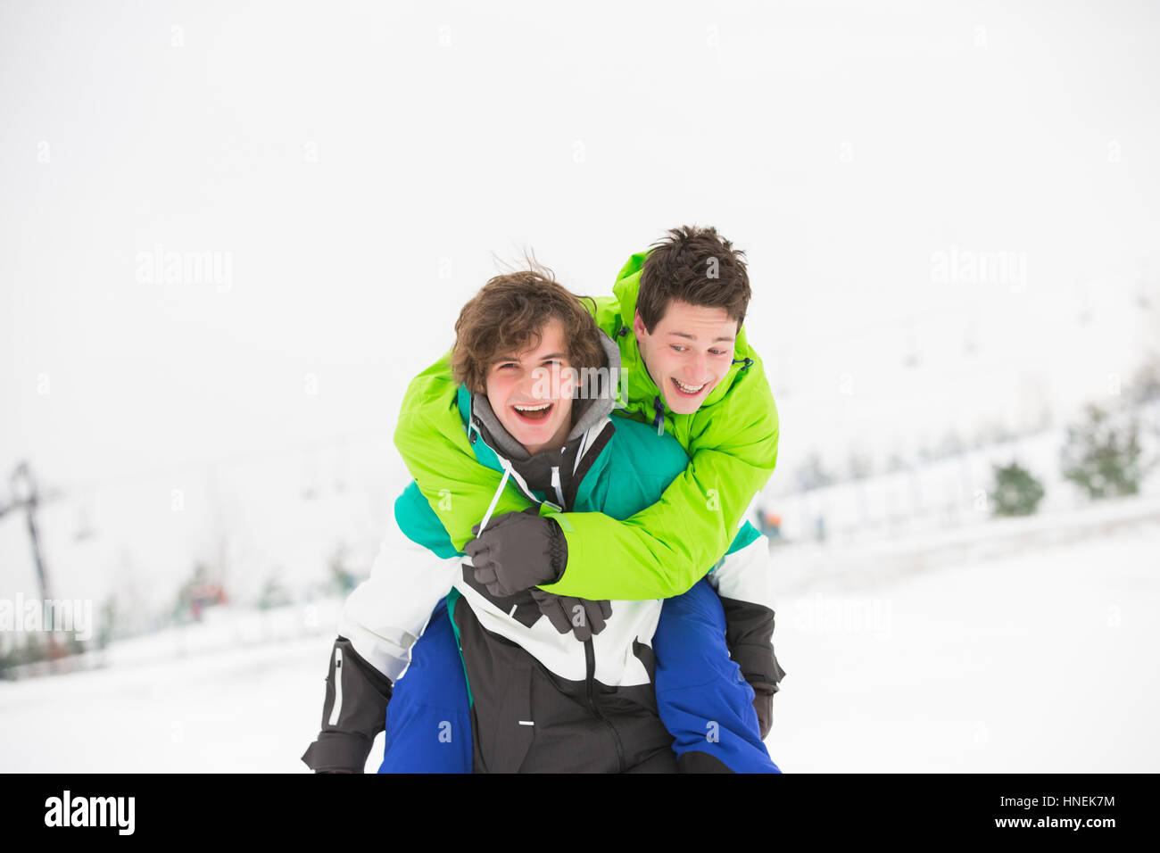 Macho joven amigos disfrutando piggyback viaje en la nieve Foto de stock