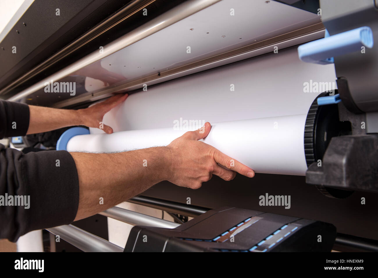 Cerca de manos del hombre blanco de gran formato de carga de rollo de papel en la impresora profesional Foto de stock