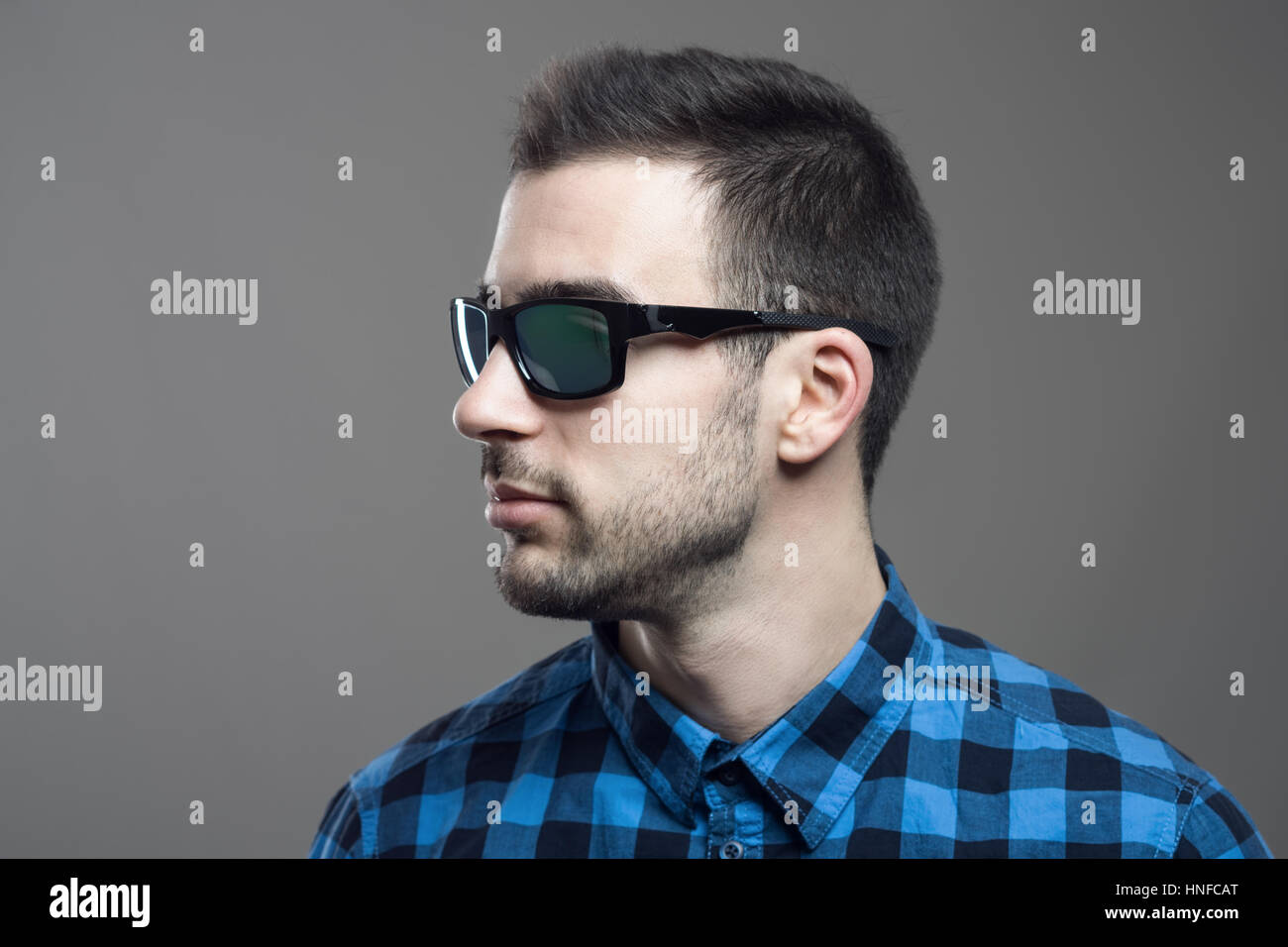 En la vista de perfil del joven hombre barbado en el Plaid shirt con gafas  de sol mirando lejos más gris de fondo de estudio Fotografía de stock -  Alamy