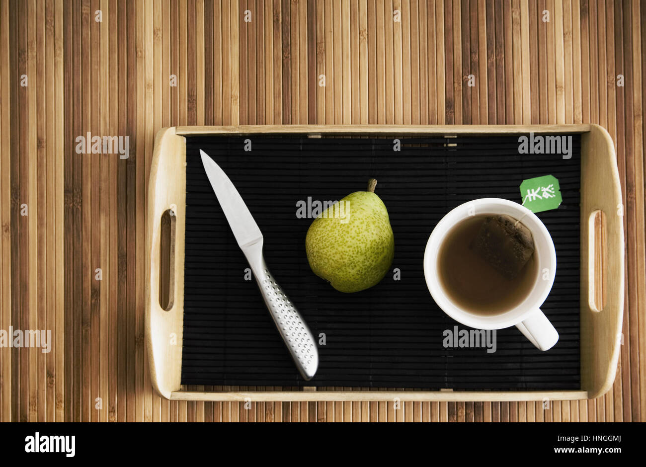 Cuchilla, pera y la taza con té en la bandeja Foto de stock