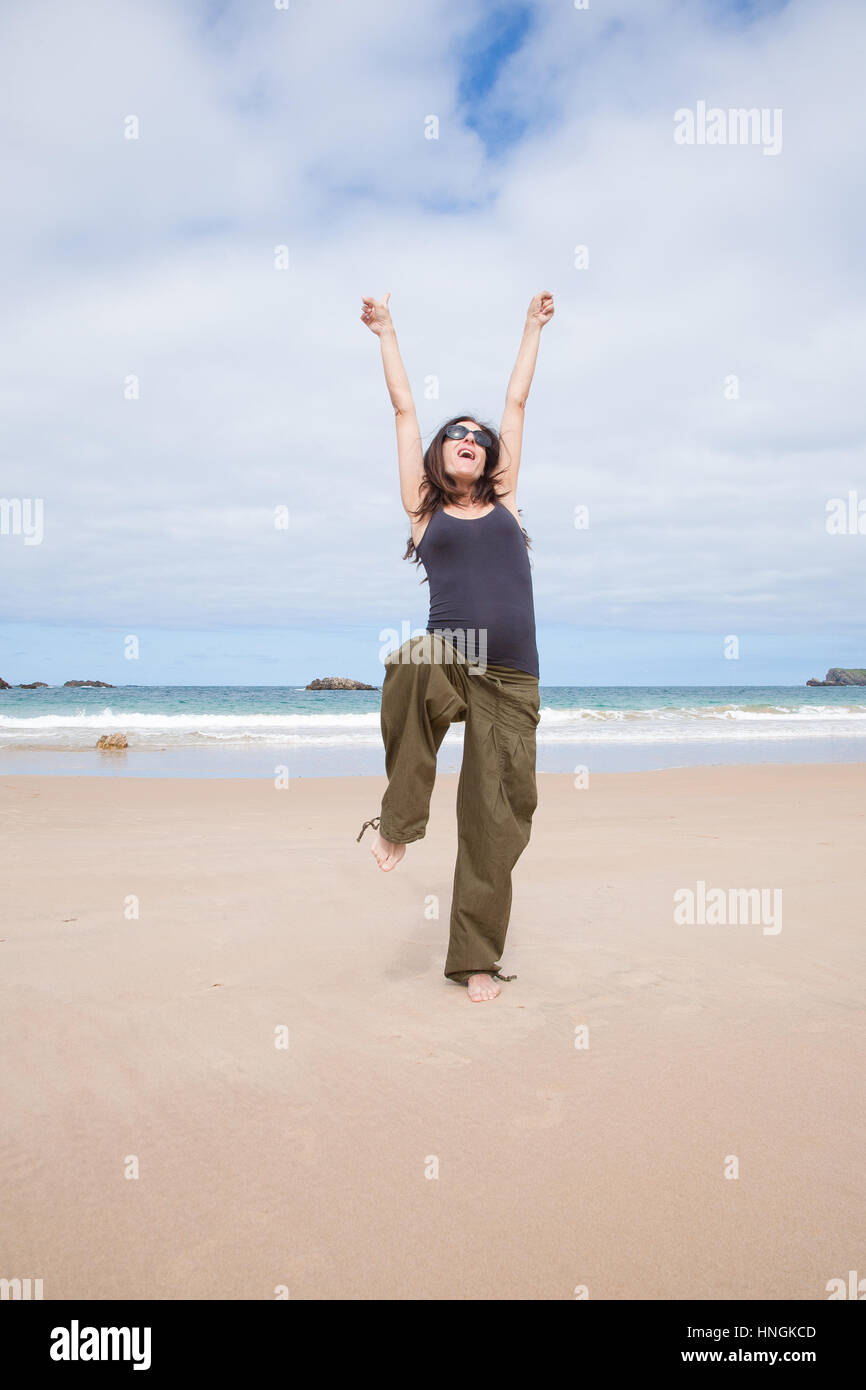 Morena de cabello marrón mujer embarazada con camisa gris y pantalón verde  gafas de sol negro feliz alegre baile en verano, en la playa de arena de  mar en Asturias Fotografía de