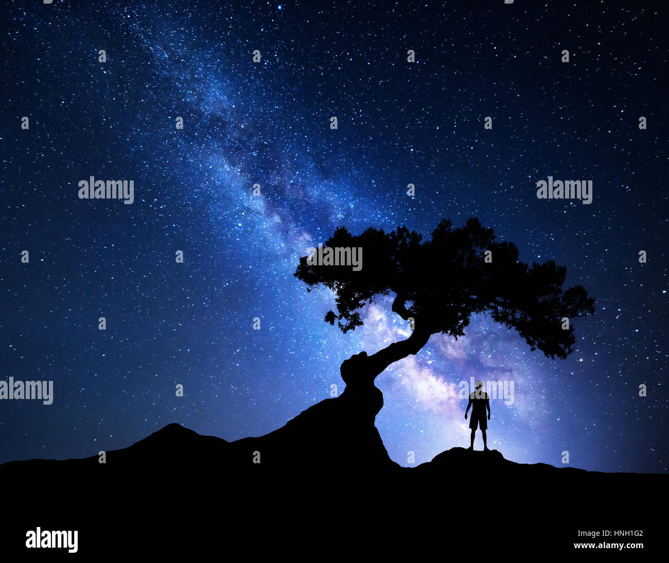 Vía Láctea. Cielo nocturno con estrellas, árbol viejo y la silueta de un hombre parado solo en la montaña. Vía láctea con luz azul y el hombre. Antecedentes de viajes Foto de stock
