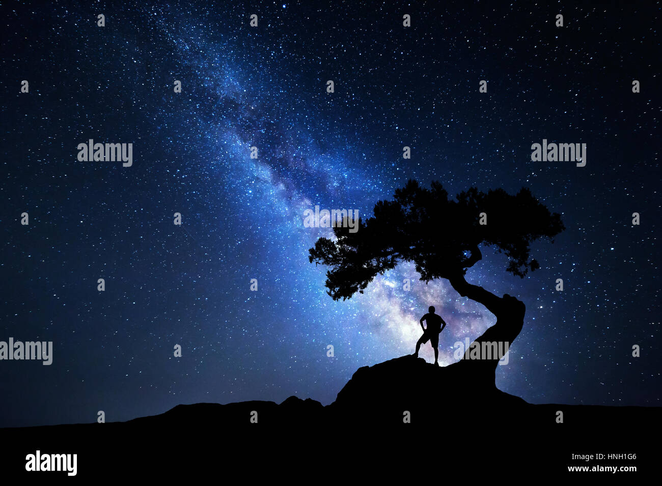 Vía Láctea. Cielo nocturno con estrellas, árbol viejo y la silueta de un hombre parado solo con mochila en la montaña. Vía láctea azul y el viajero. Viajes ba Foto de stock