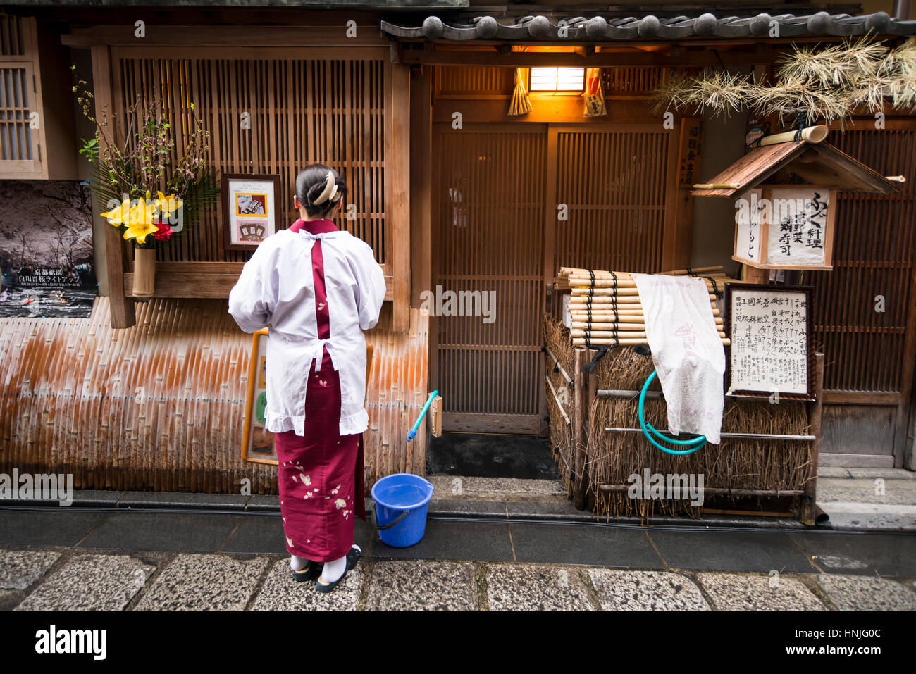Una trabajadora de limpieza de entrada antes de abrir el restaurante, Distrito Gion, Kioto, Japón Foto de stock