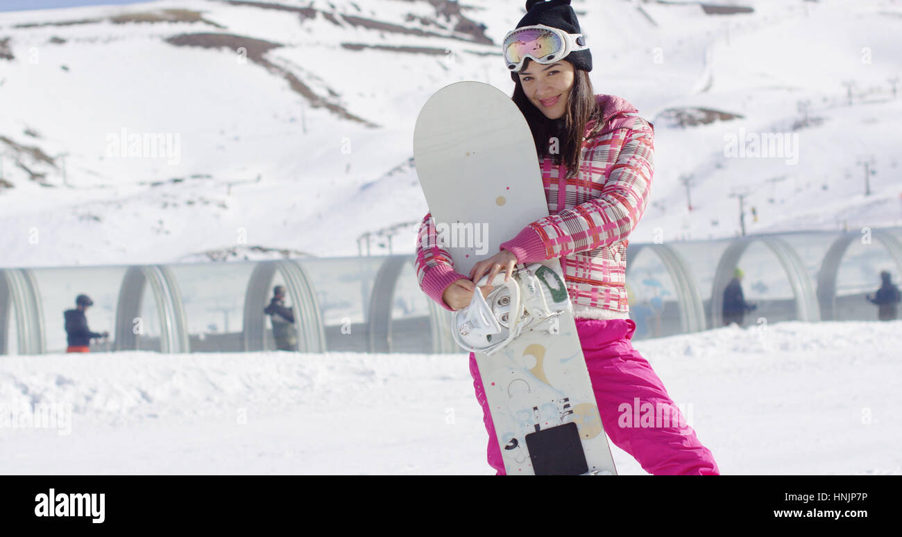 joven mujer con nieve pendiente sosteniendo su snowboard. Sonríe a la cámara. Vestían de esquí Rosa y gafas. Disfruta de vacaciones de invierno Fotografía de stock - Alamy