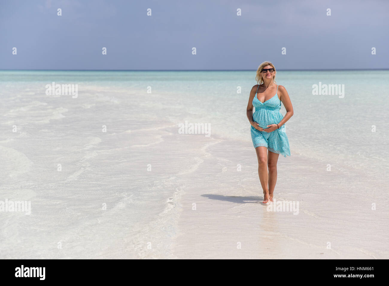 La mujer embarazada está sosteniendo su vientre y caminar sobre el banco de arena Foto de stock