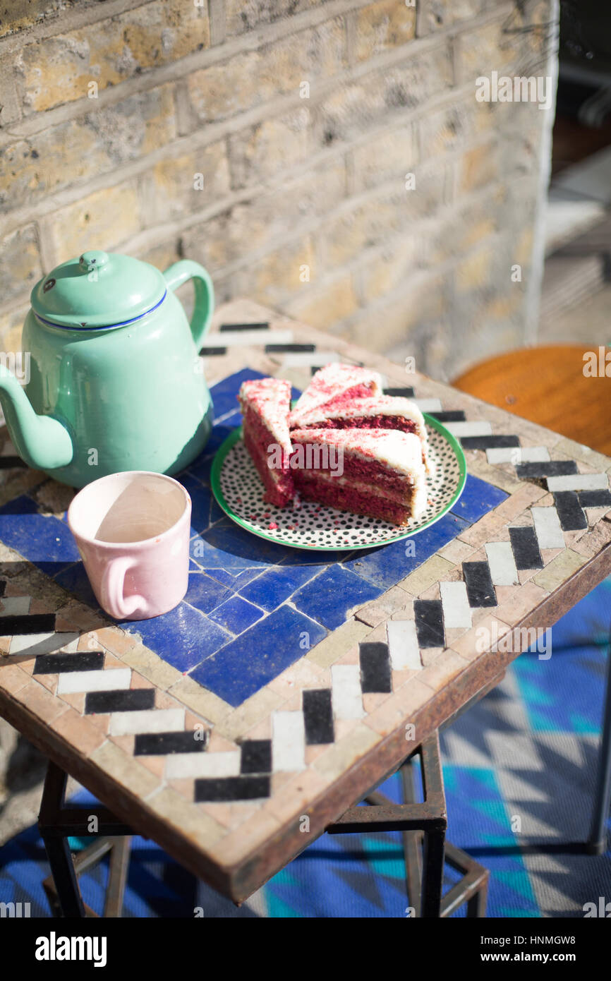 Té y bizcocho fuera sobre una mesa de jardín por un muro de ladrillo Foto de stock