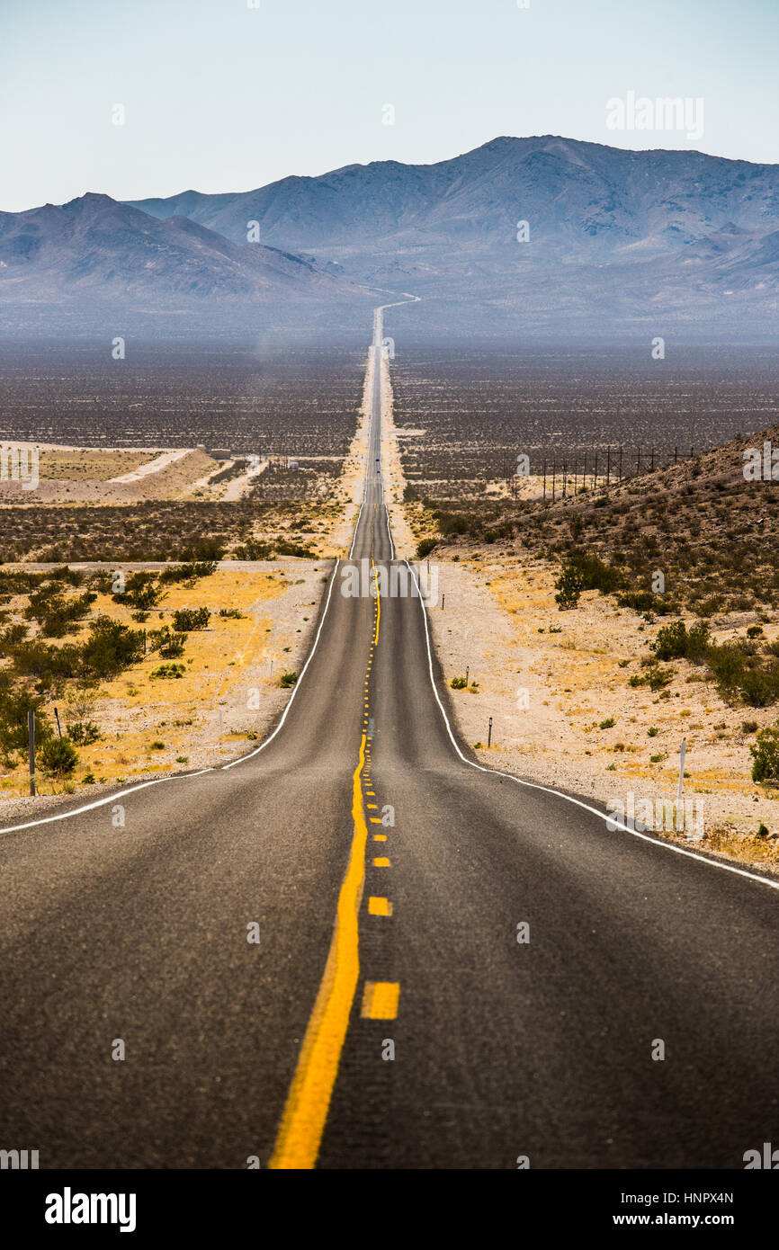 Classic vista vertical de una interminable carretera recta atravesando el paisaje árido del famoso Valle de la muerte en un día soleado de verano, California, EE.UU. Foto de stock