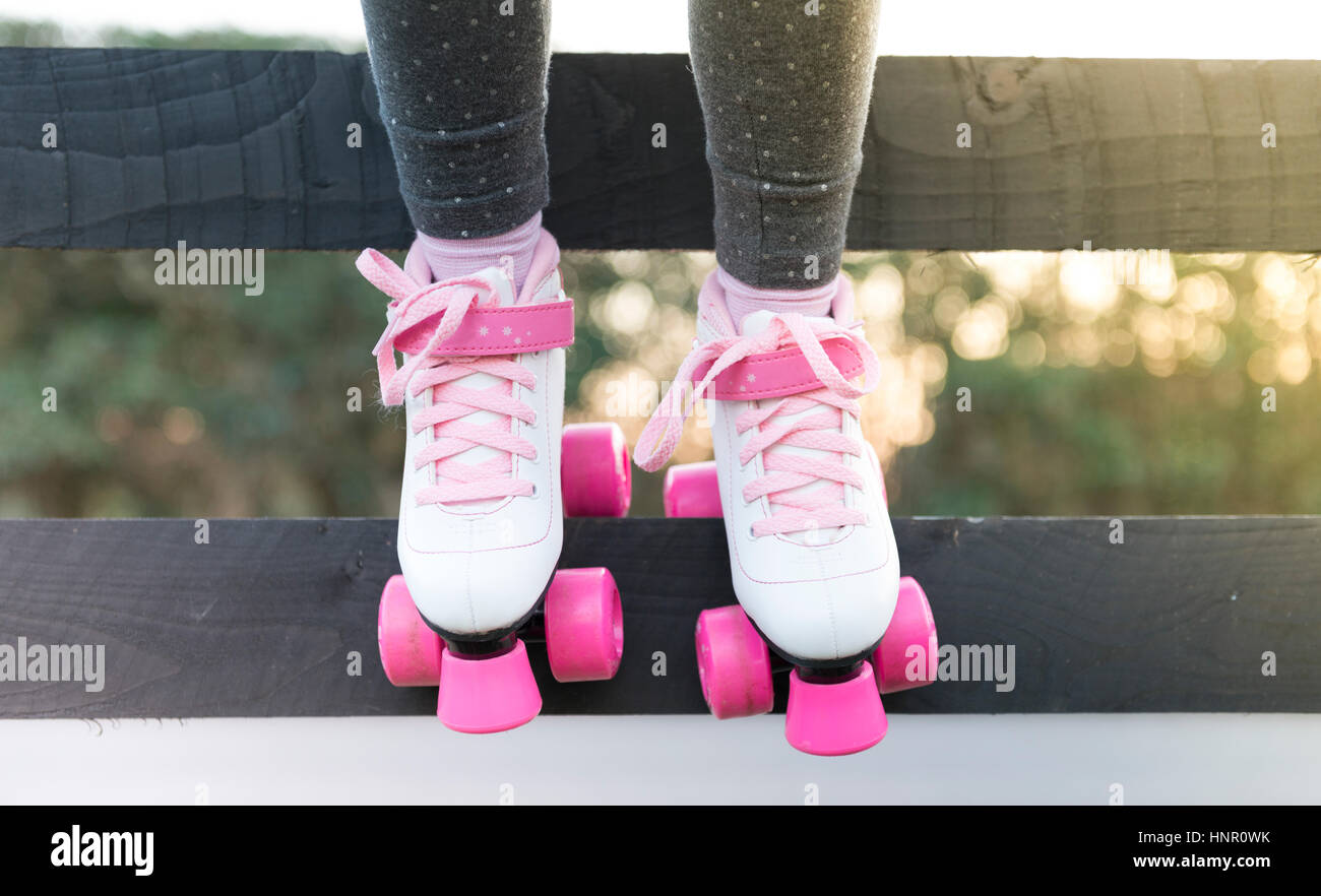 Una niña sentada sobre una valla en patines Foto de stock
