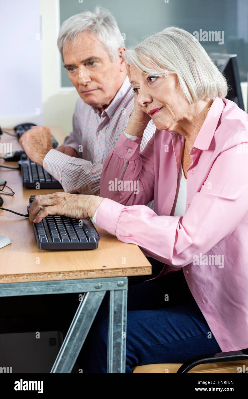 Aburrido mujer mayor uso del ordenador con machos classmate Foto de stock
