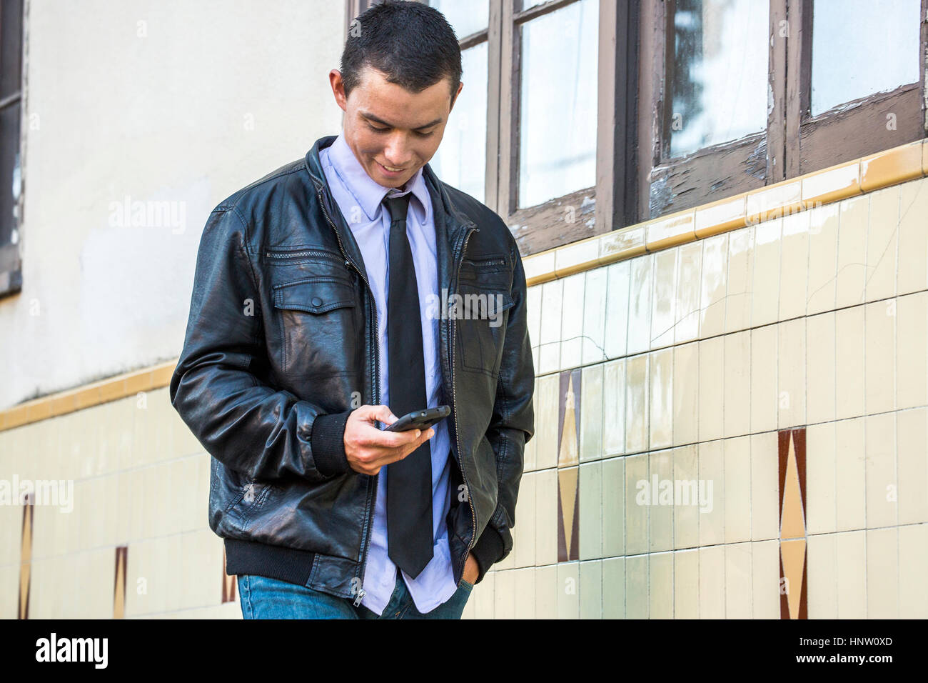 Raza mixta hombre vestido con chaqueta de cuero por mensajería de texto en el teléfono celular Foto de stock