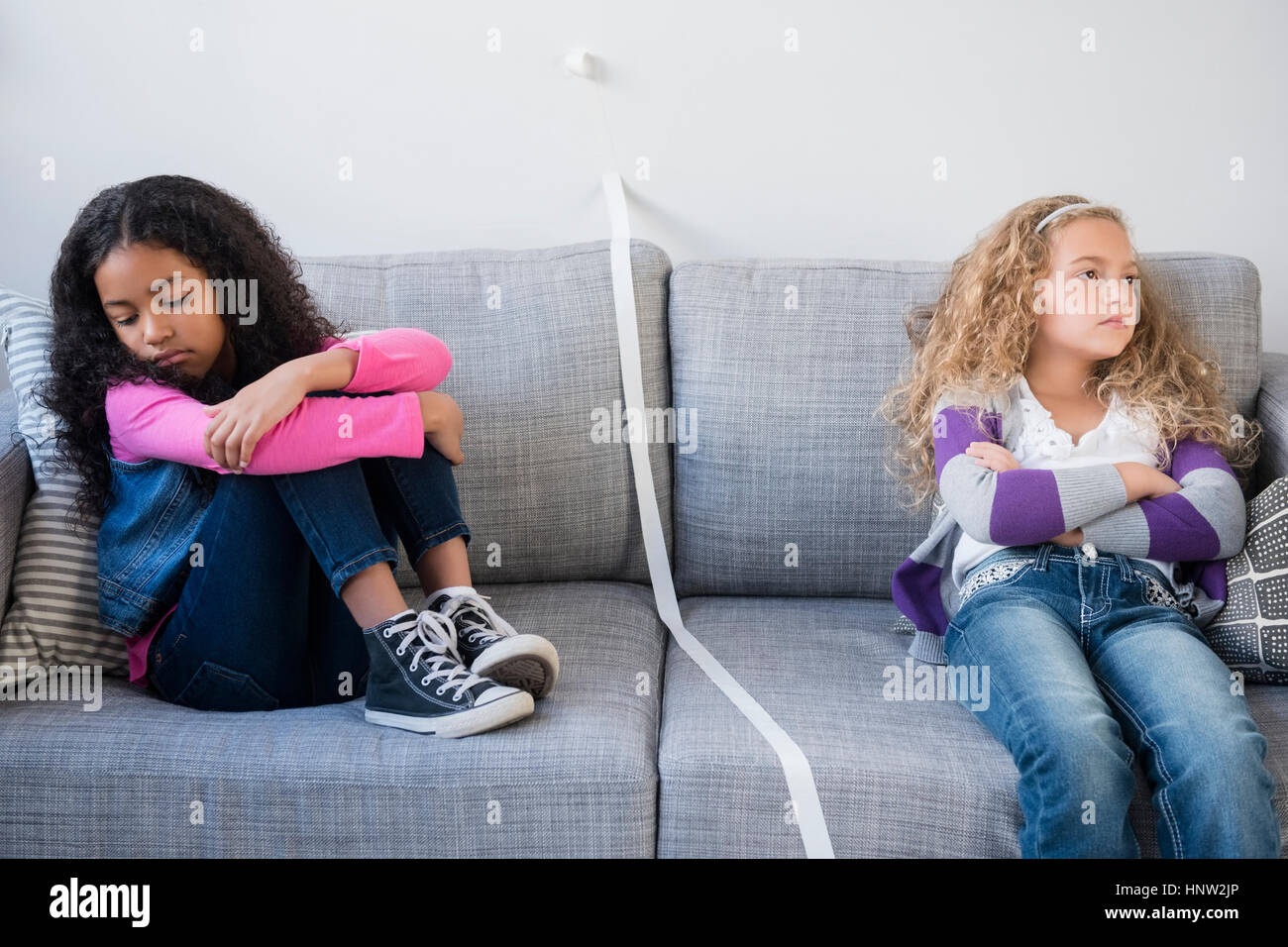 Frustrado niñas dividiendo sofá con cinta adhesiva. Foto de stock