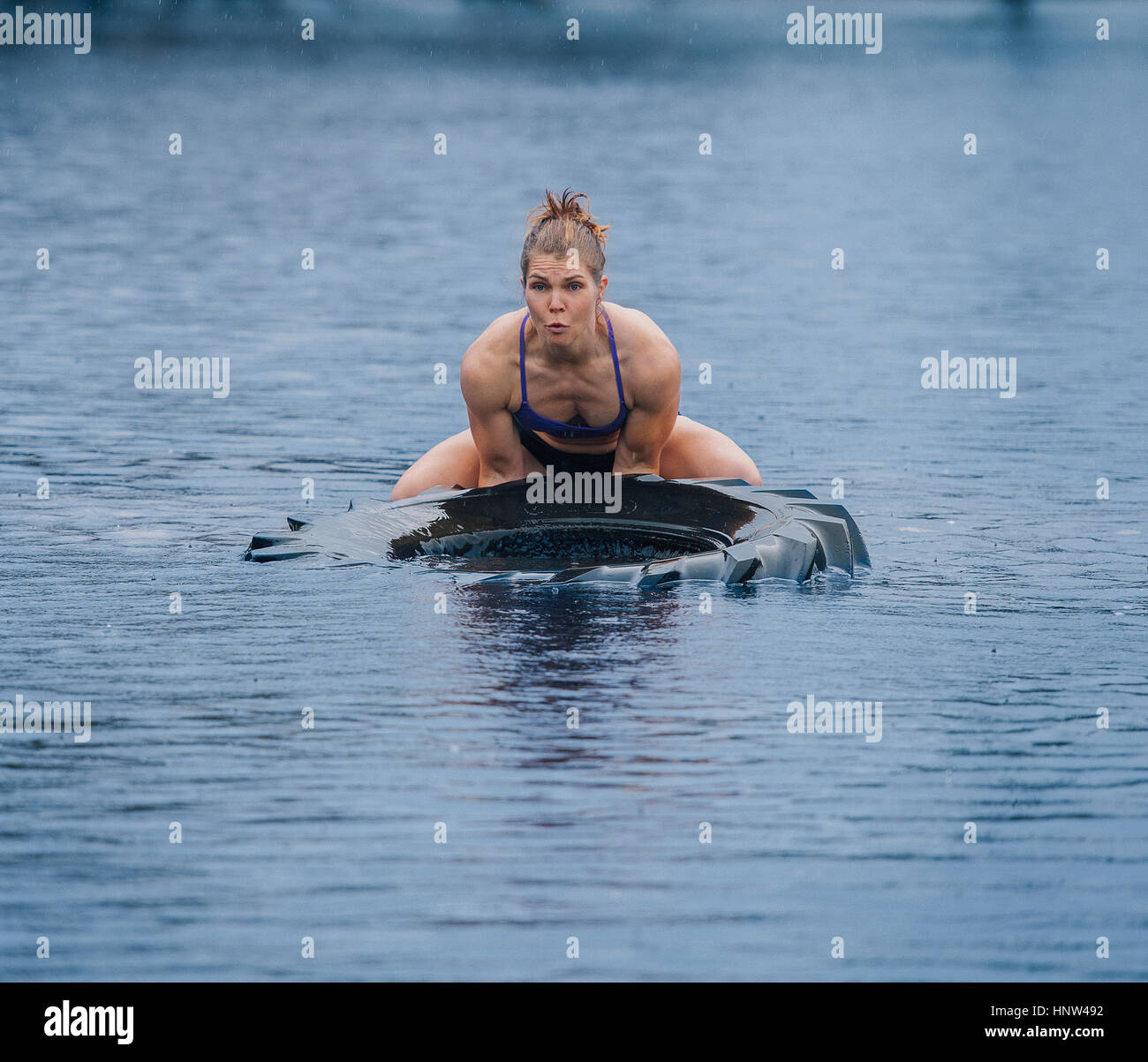 Mujer caucásica levantar pesadas neumático en el lago Foto de stock