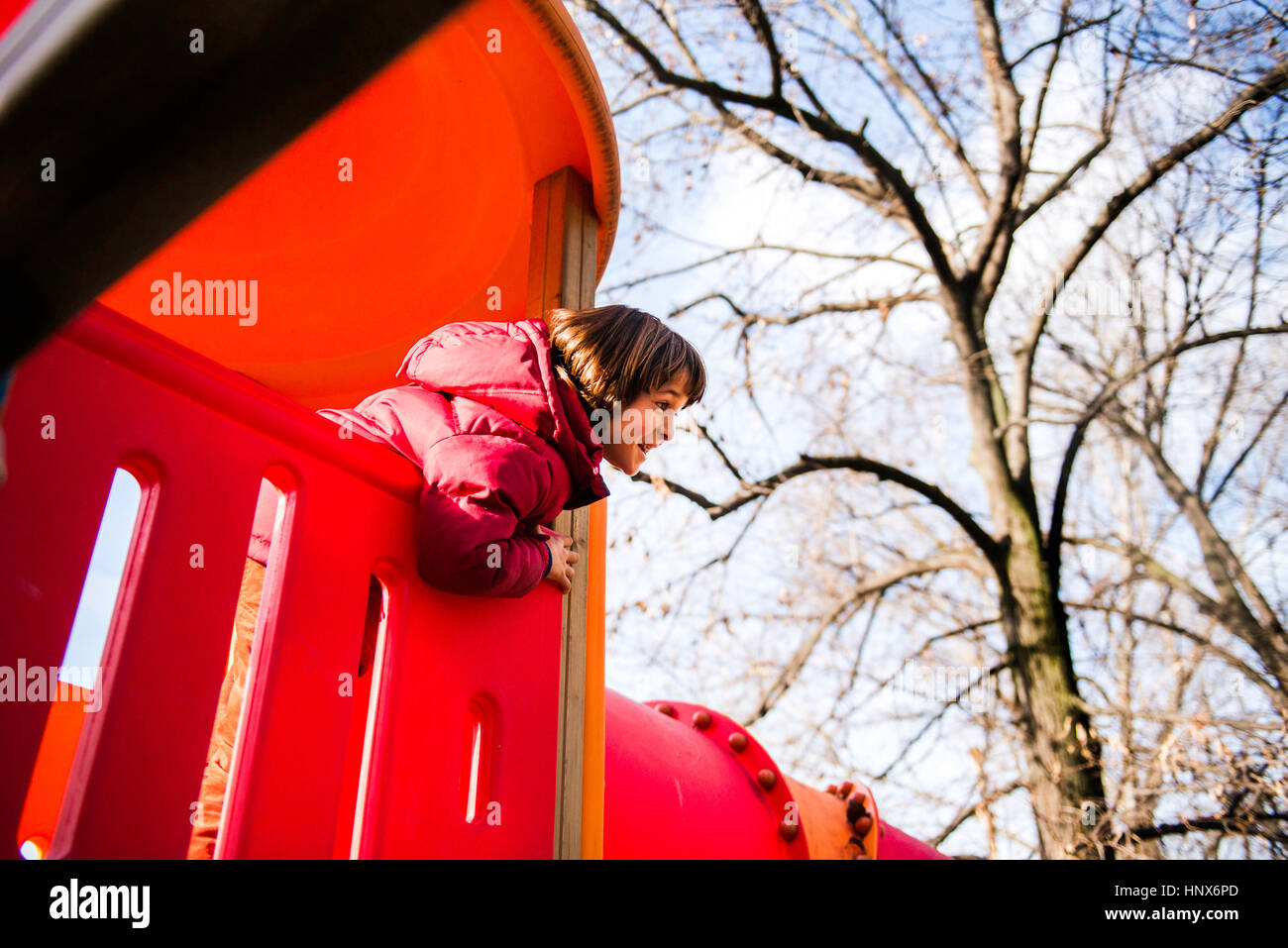 Niño mirando hacia fuera desde la parte superior de la diapositiva playground rojo Foto de stock