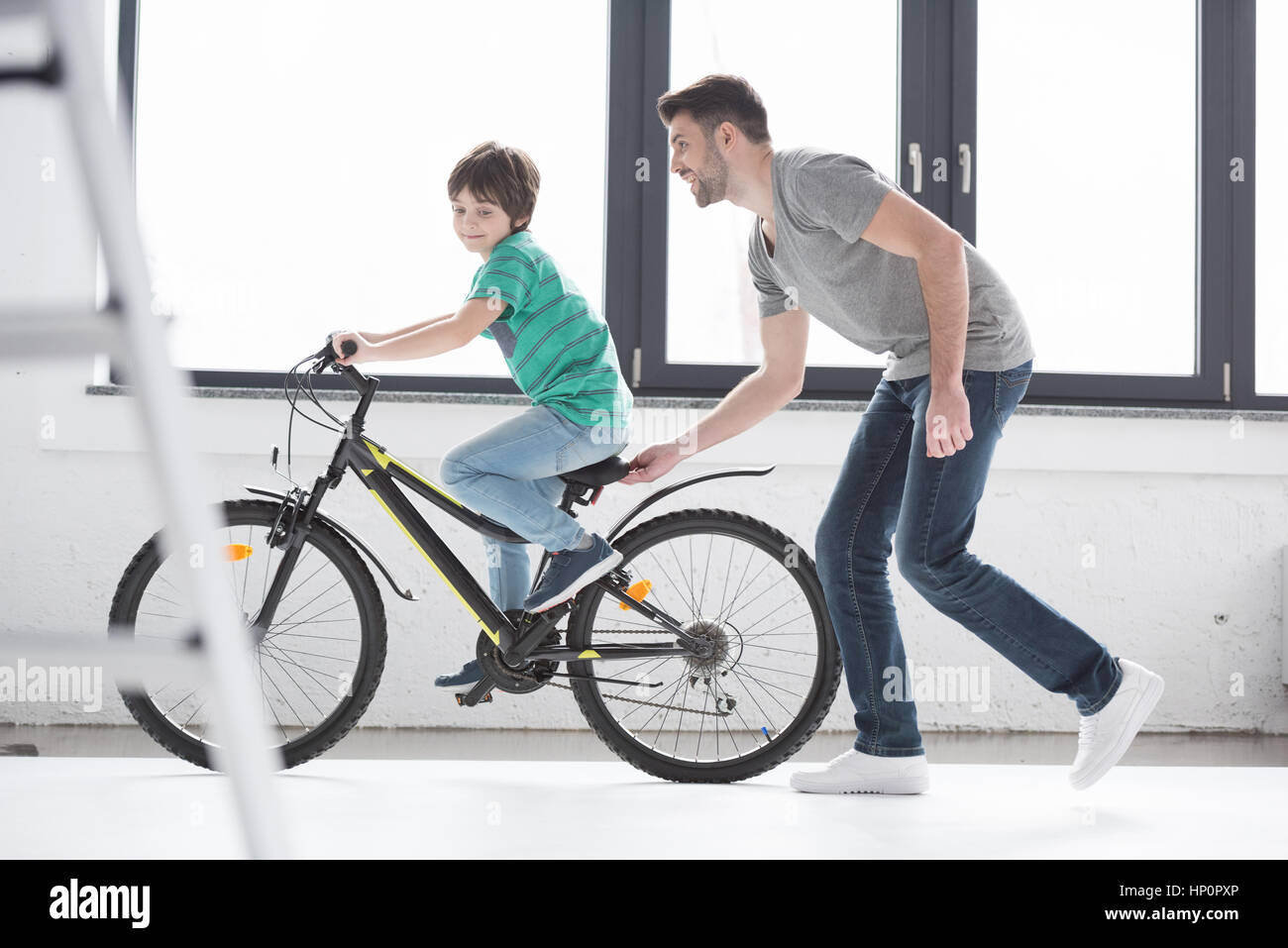 Padre joven ayudando al hijo a andar en bicicleta Foto de stock