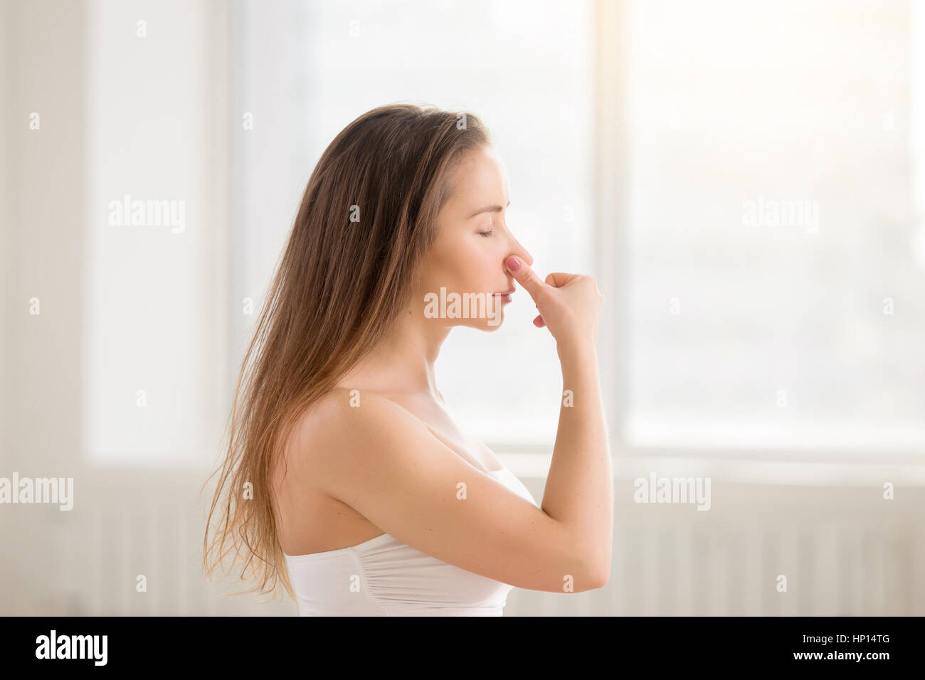 Atractiva mujer joven hacer suplentes fosa nasal respiratoria, blanco Foto de stock