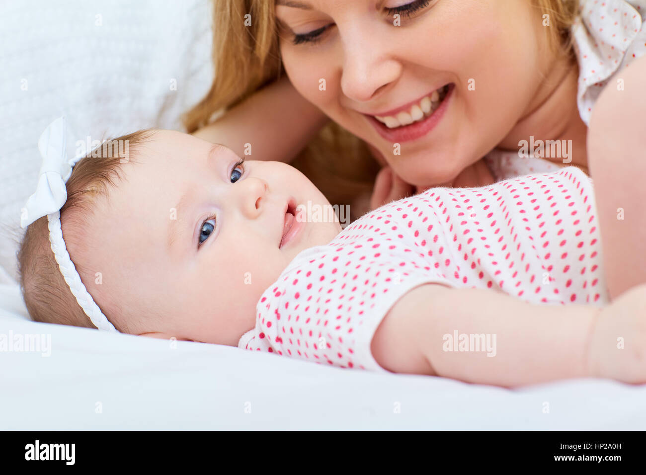 Madre jugando con su bebé en la cama. Mamá sonríe a su hijo Foto de stock