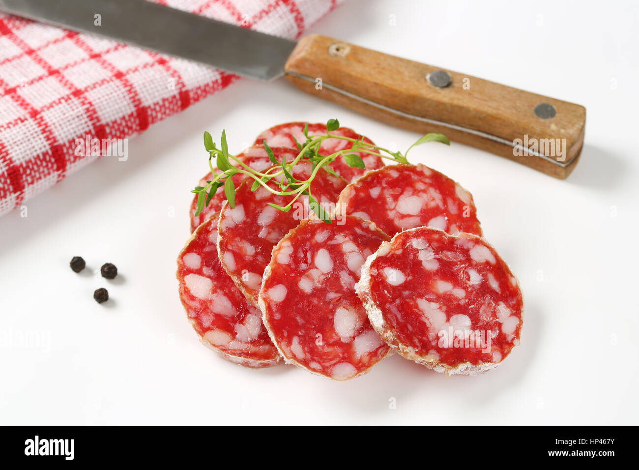 Cerca del francés rodajas de salami seco, cuchillo de cocina y especias sobre fondo blanco. Foto de stock