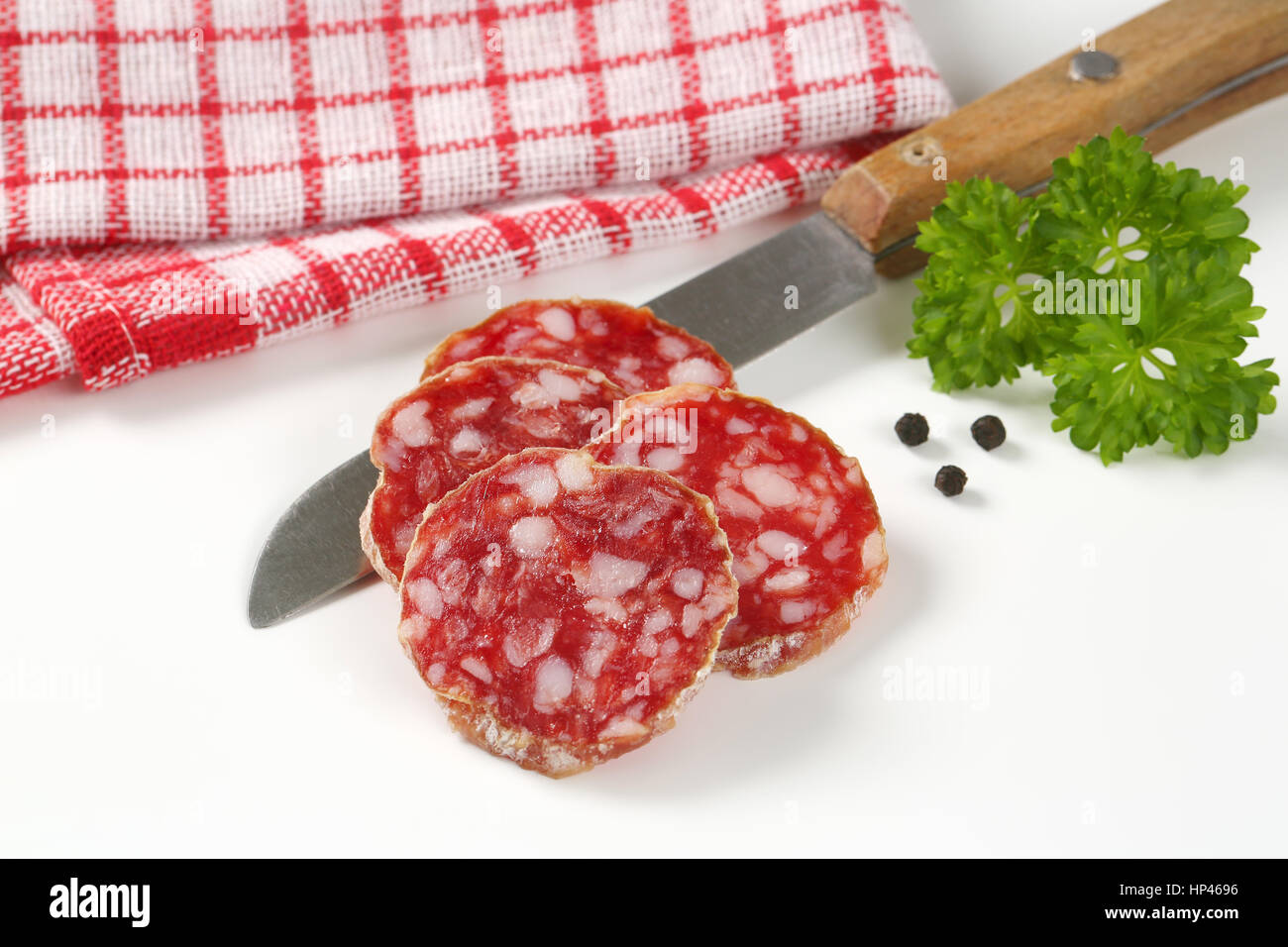 Cerca del francés rodajas de salami seco, cuchillo de cocina y especias sobre fondo blanco. Foto de stock