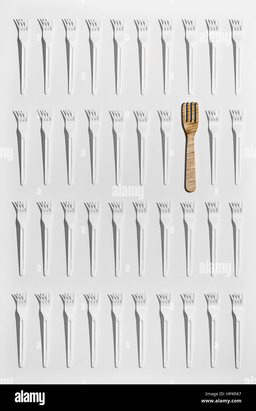 Muchos tenedores de plástico desechable y 1 de madera artesanal, conceptos: uno de un tipo, ser diferente, distinguirse, natural y artificial Foto de stock