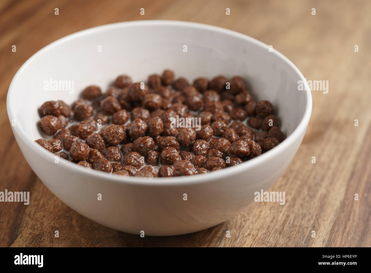 Las bolas de cereales de chocolate con leche en el recipiente blanco para desayunar en la mesa de madera, enfoque superficial Foto de stock