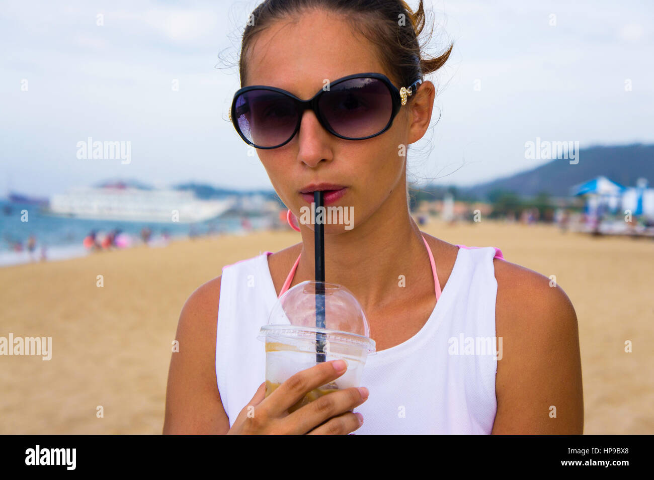 Chica con gafas de sol bebiendo café con una pajita en un vaso de plástico  en la playa cercana Fotografía de stock - Alamy
