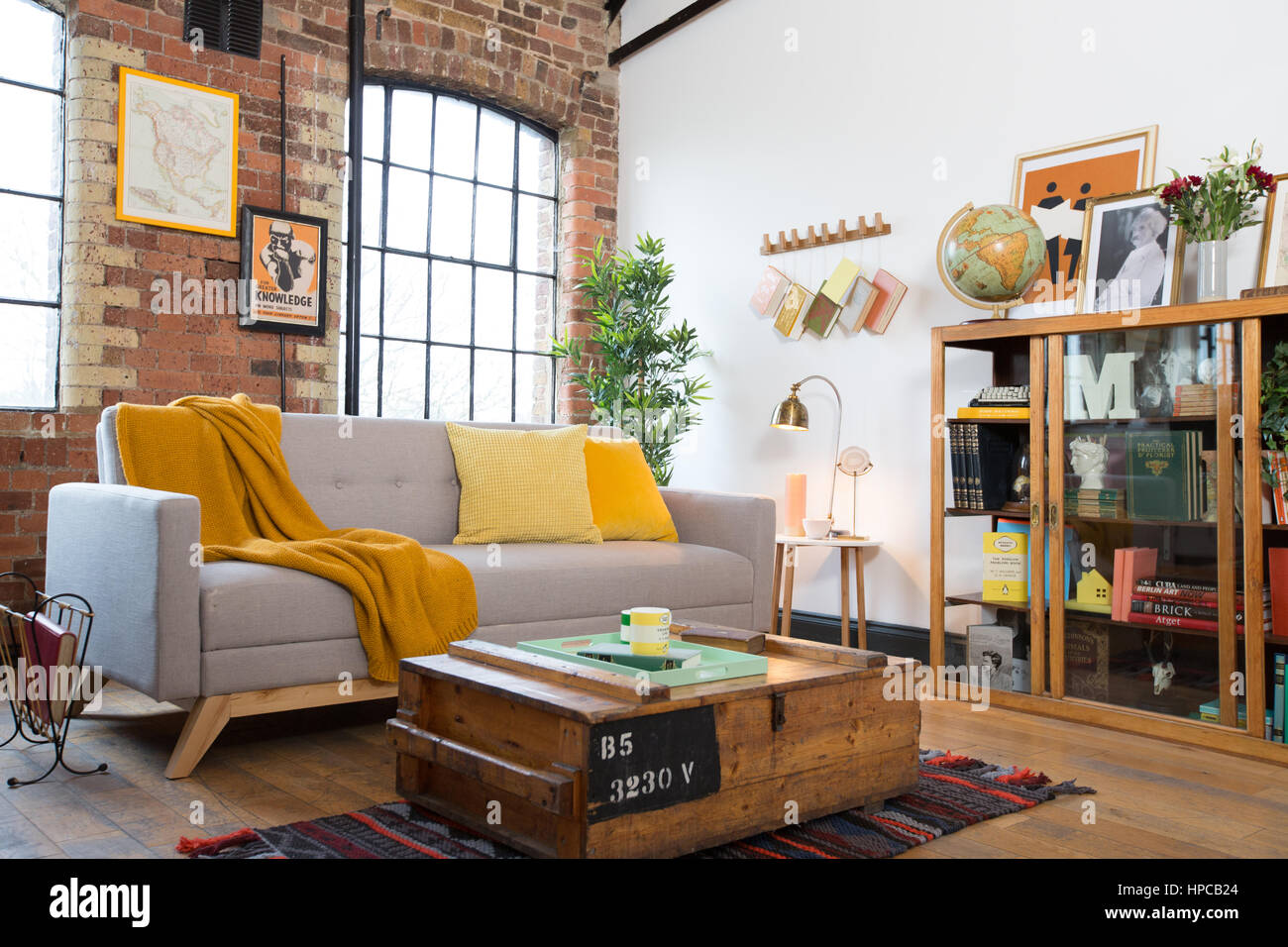 Un salón con paredes de ladrillo a la vista y un diseño danés gris amarillo sofá con una manta y cojines Foto de stock