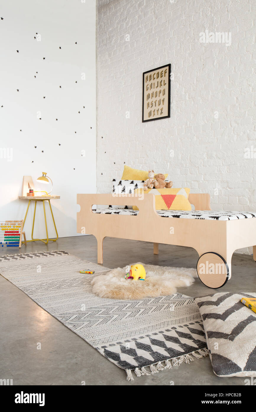 Una cama en un dormitorio infantil con paredes blancas y piso de concreto Foto de stock