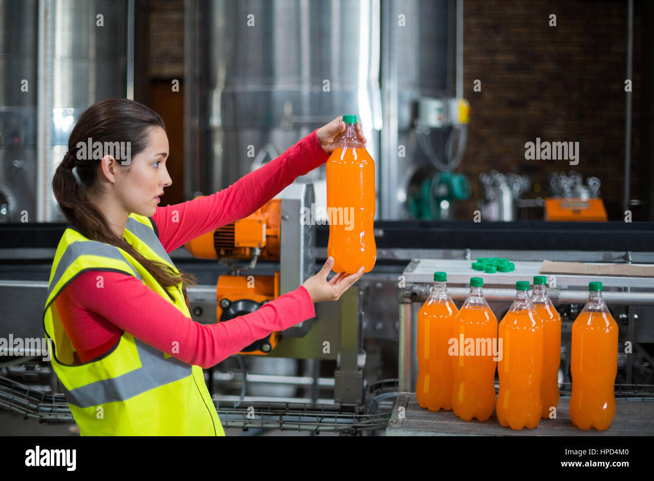 Trabajador de fábrica femenina examinando una botella de jugo en la fábrica. Foto de stock
