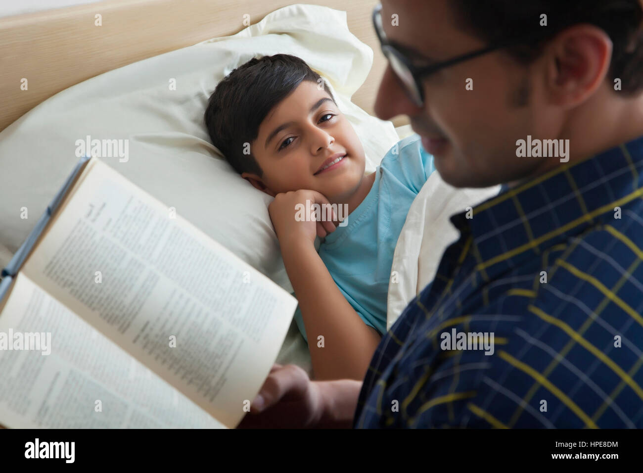 Padre leyendo un libro a su hijo en el dormitorio Foto de stock