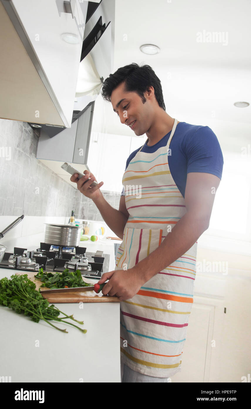 Joven picar las verduras y utilizando un teléfono móvil Foto de stock