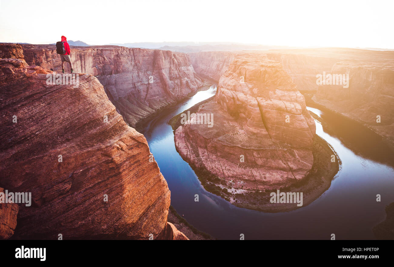 Un hombre caminante está de pie sobre acantilados disfrutando de la hermosa vista del río Colorado fluye a famoso Horseshoe Bay tienen vistas al atardecer, Arizona Foto de stock