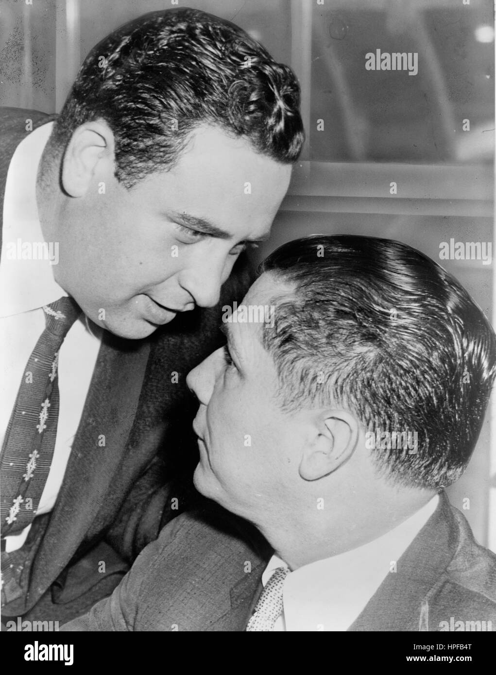 Wiretap experto Bernard Spindel susurra en el oído de James Hoffa R después de la sesión del tribunal en la que se declaró inocente de los cargos de escuchas telefónicas ilegales, New York, NY, 1957. Foto de stock