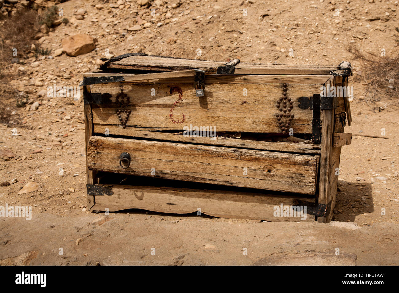 Un tiempo gastado pecho antiguo de madera utilizada como un puesto en el mercado. Rodeado de polvo y rocas. Decorado con cuero y correas de metal. Foto de stock