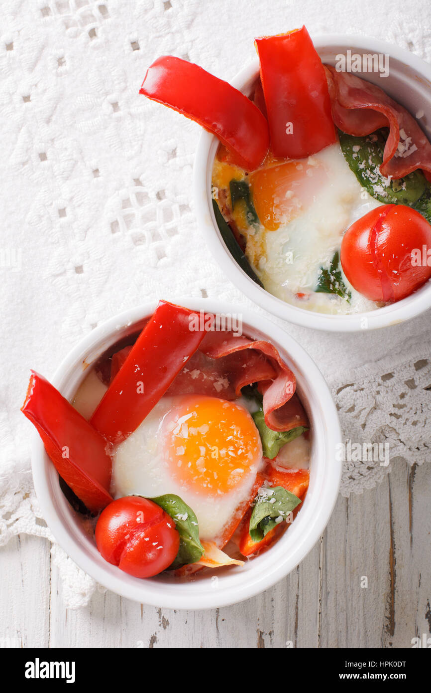 Huevo frito con espinacas, pimientos, tomates y queso en una taza de cerca en la tabla. vista vertical desde arriba Foto de stock
