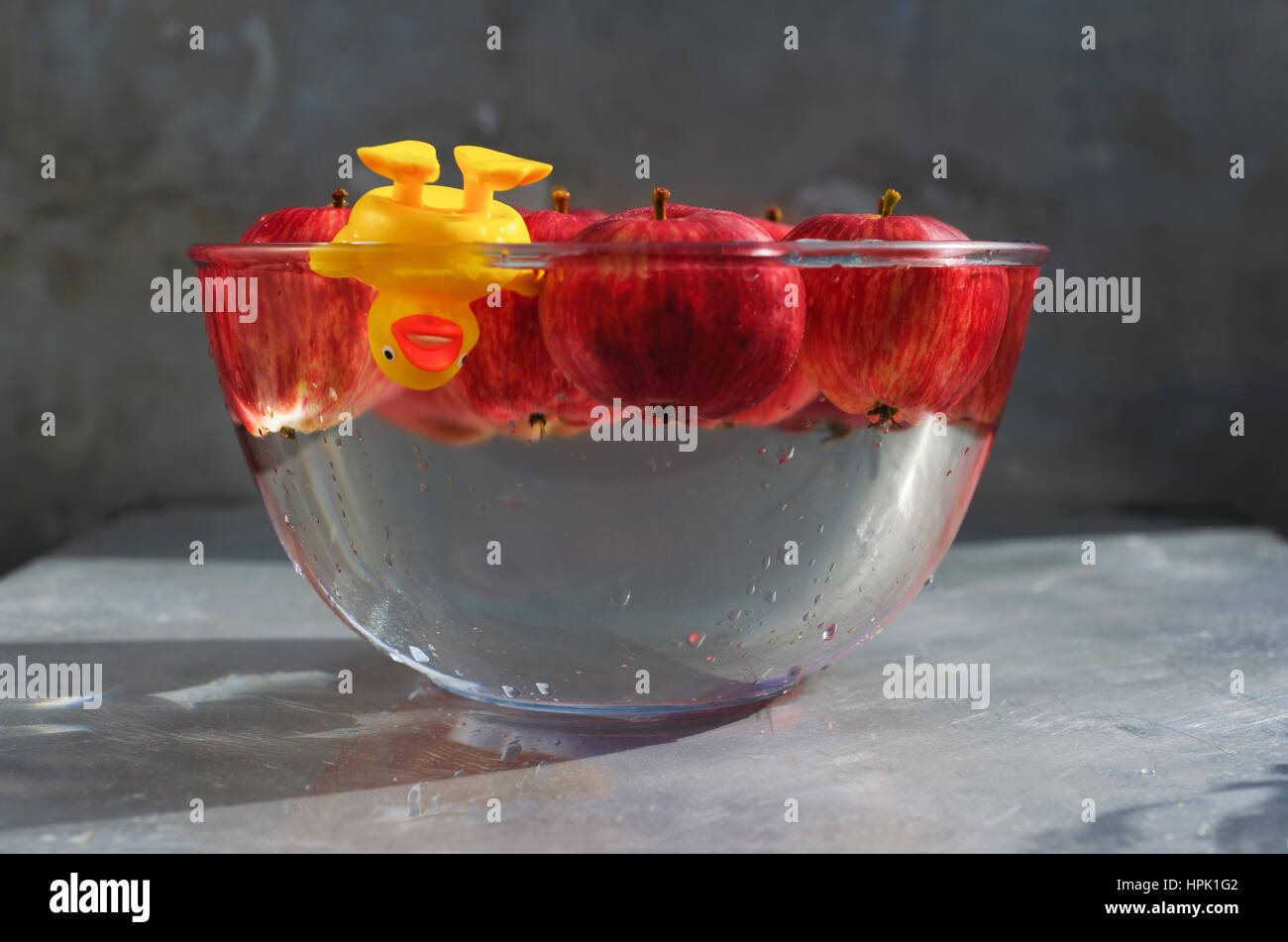 Ducking para las manzanas. Pato de plástico amarillo disfrutando de un buen zambullirse en un tazón de agua y manzanas rojas. Foto de stock