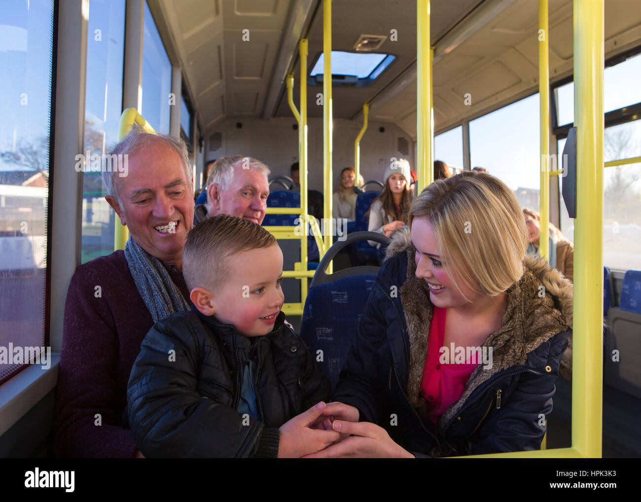 Madre sola con su padre y su hijo en el autobús. El muchacho está sentado sobre las rodillas de su abuelo con su madre manteniendo sus manos. Foto de stock