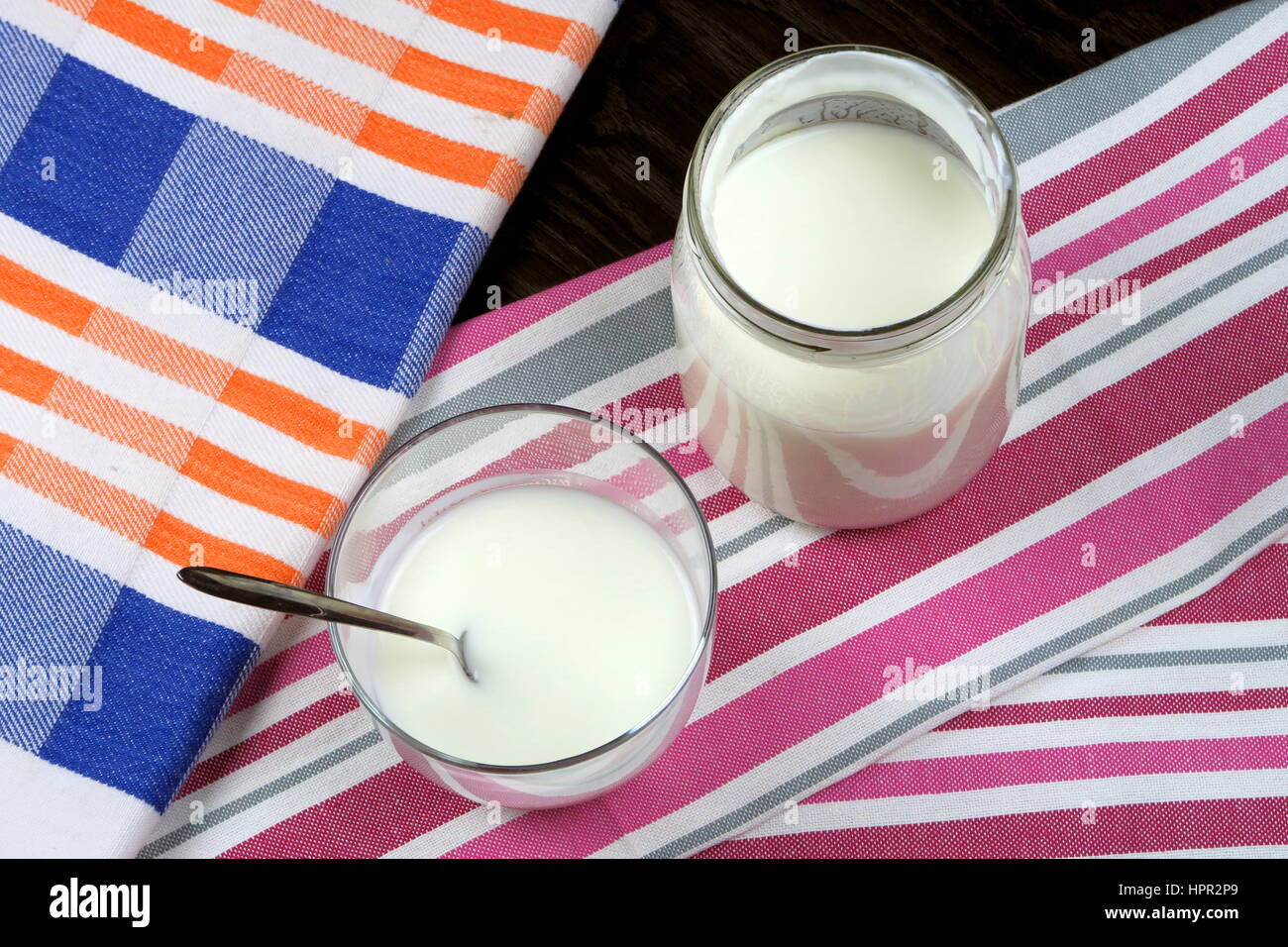 Orgánicas caseras Yogur natural bajo en grasa en un vidrio claro (y jar) con cucharilla en coloridos trapos de cocina desde arriba - alimentación natural de vida verde Foto de stock