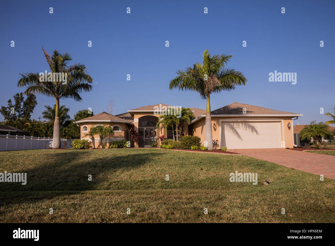 El suroeste de Florida típico de bloque de hormigón de estuco y casa en el campo, con palmeras, plantas tropicales y flores, césped y pinos. f Foto de stock
