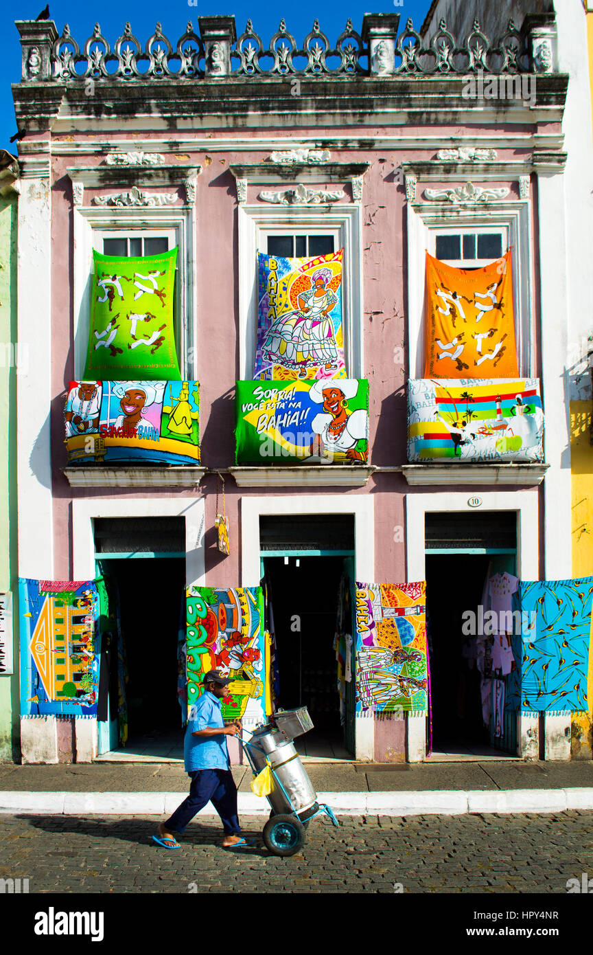 Una escena de Pelourinho, en Salvador, Brasil. Un vendedor callejero que está empujando su carrito, vibrante y mantas multicolores están colgados en un almacén de la fachada. Foto de stock