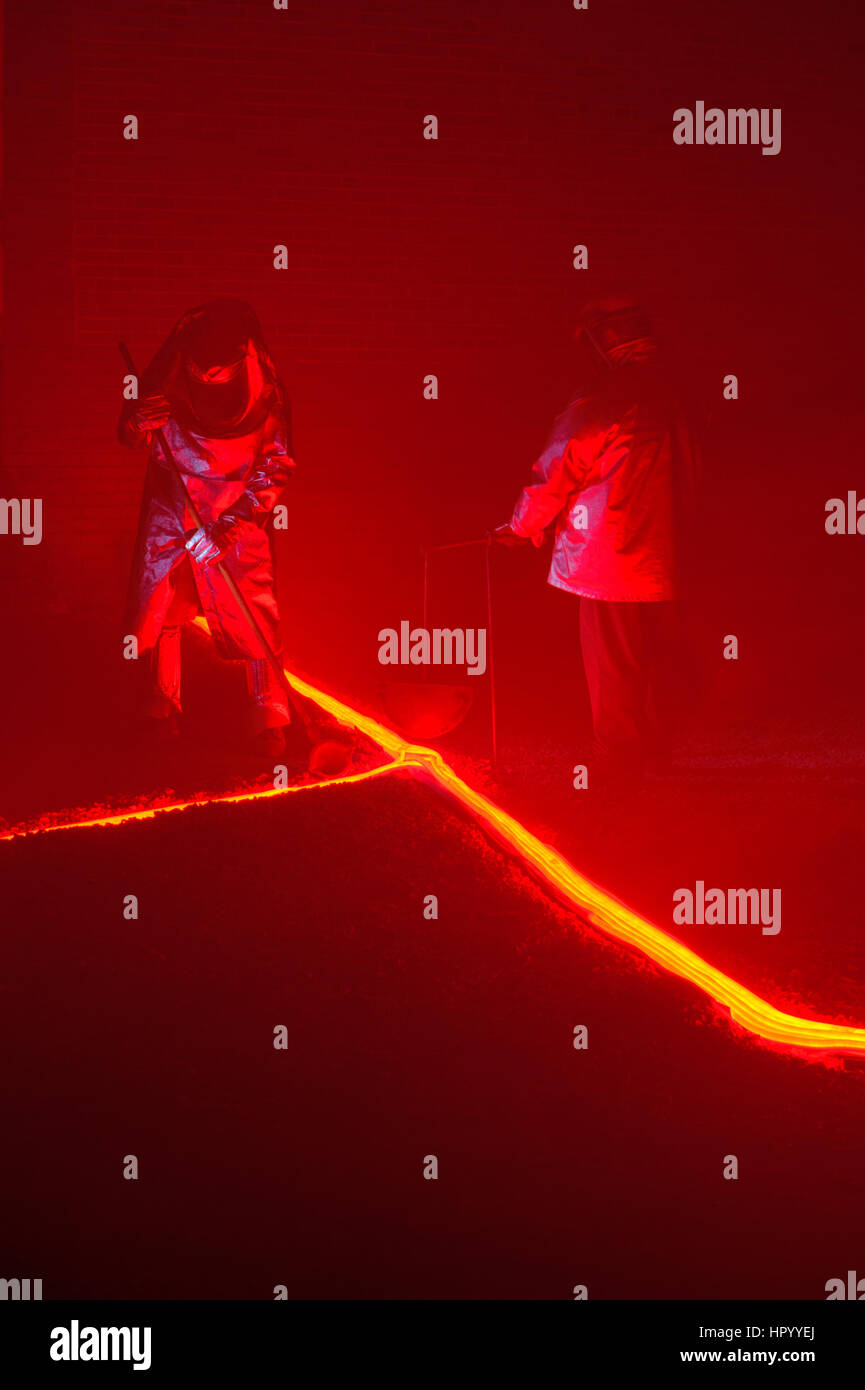 Verter caliente, incandescente, hierro fundido en un suelo de barro por dos steelworkers, dos recreadores recreando un proceso metalurgical. Foto de stock