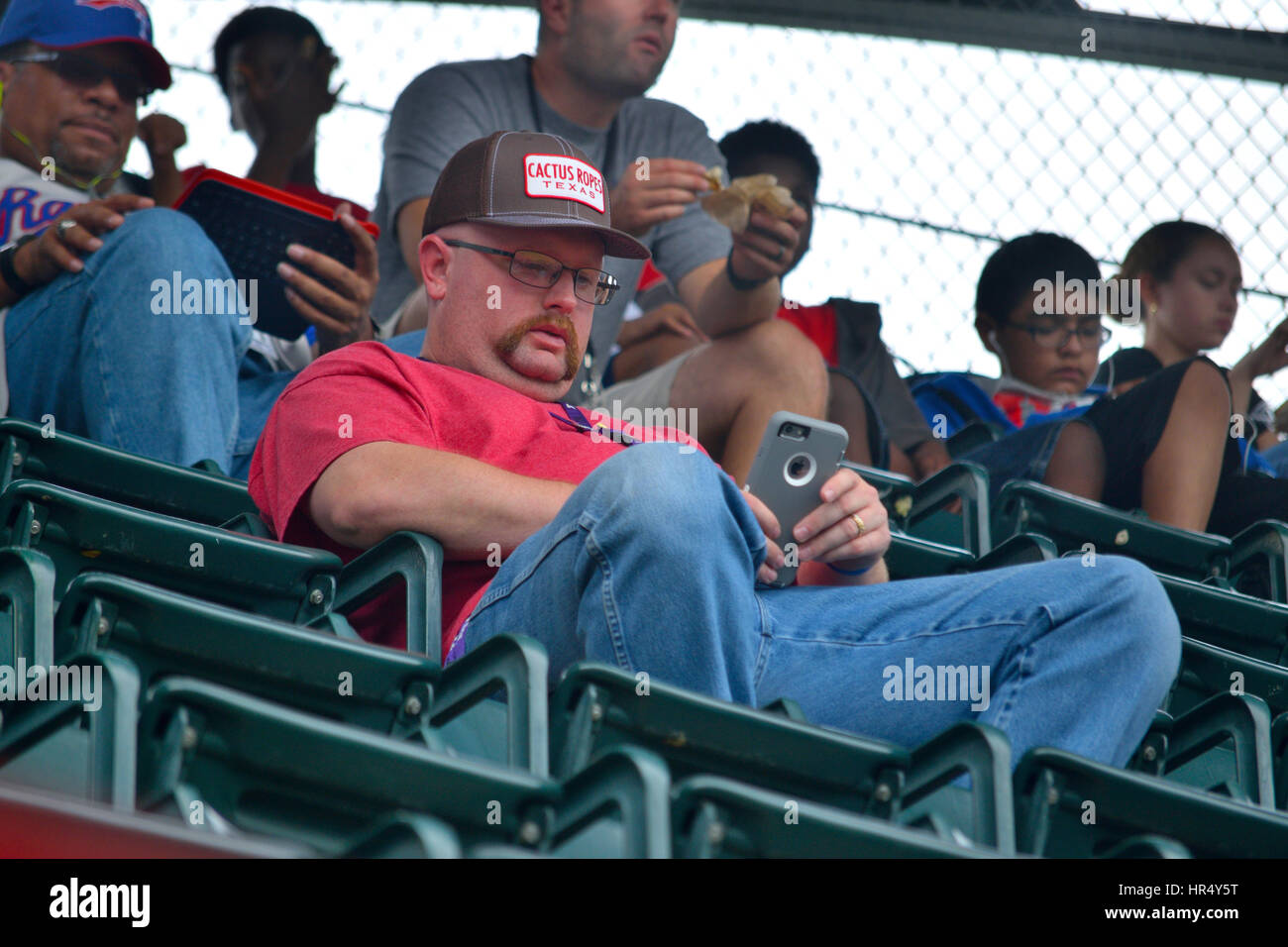 Un hombre en un evento deportivo de texto en su teléfono en lugar de ver el juego. Foto de stock